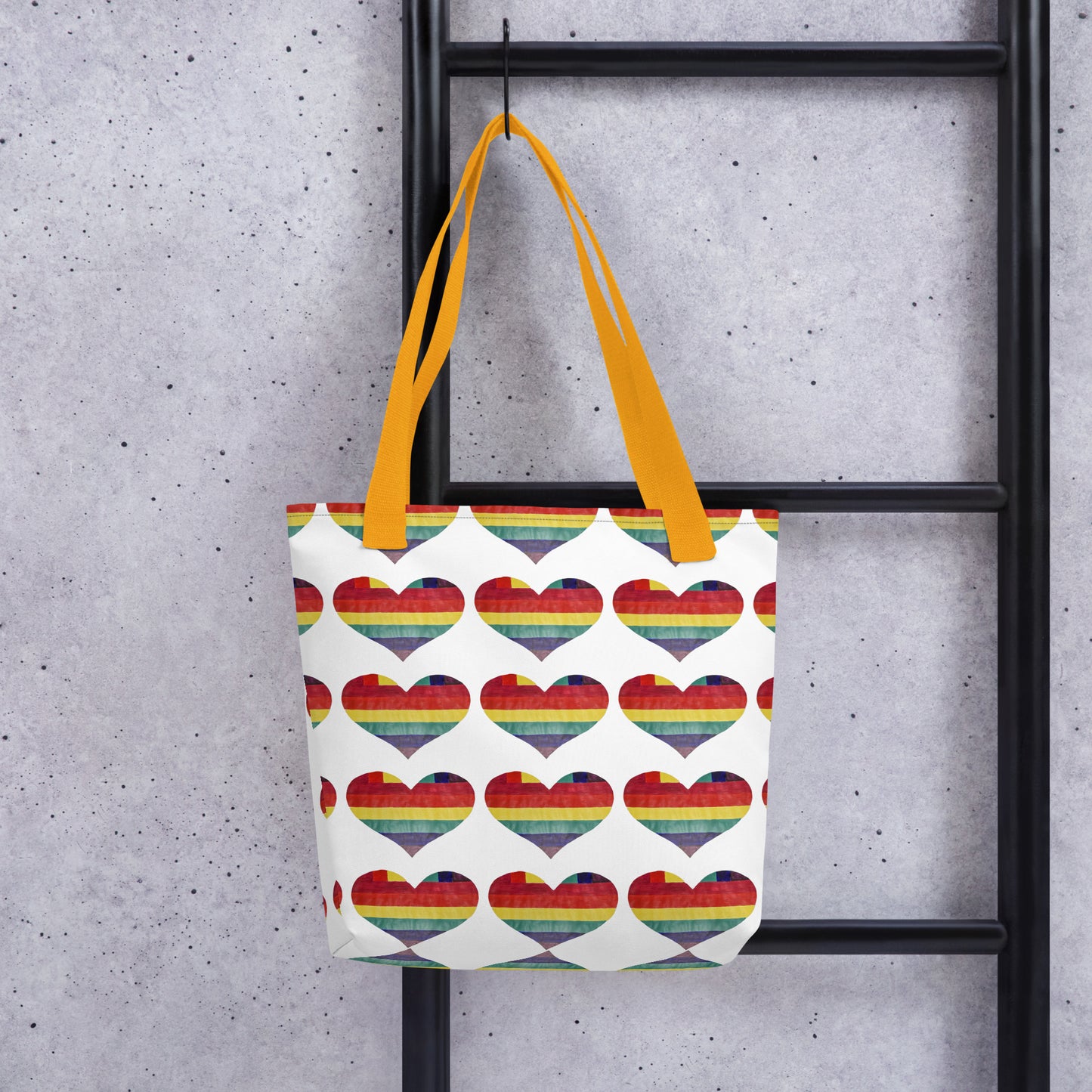 LGBT pride tote bag with rainbow heart pattern and yellow handles hanging on black metal ladder