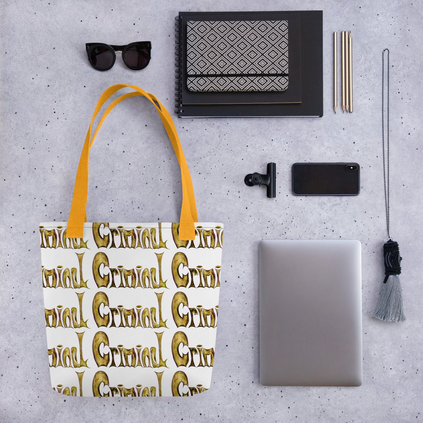 Stylish shopping tote CRIMINAL PRINT with yellow handles alongside sunglasses, notebook, phone, laptop, and pencils