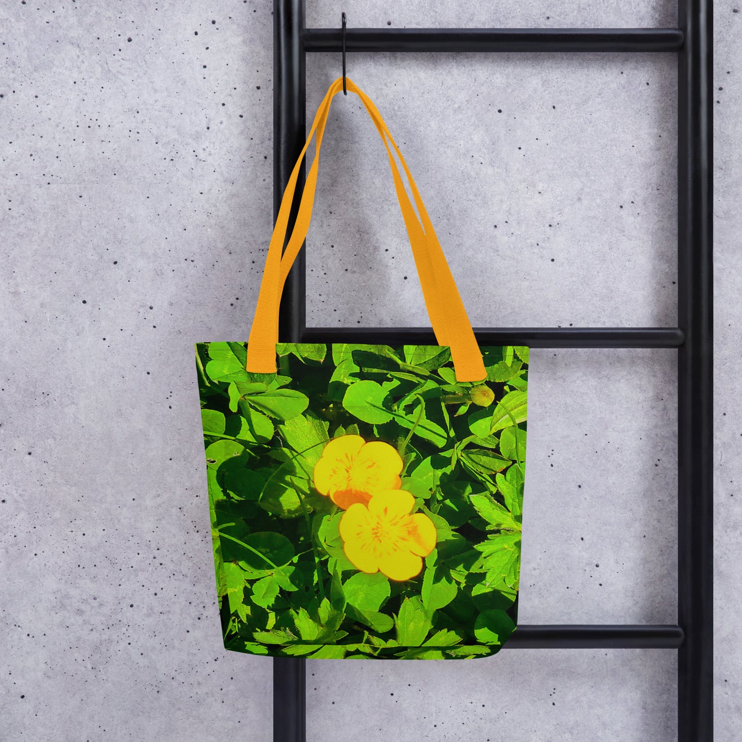 Summer beach tote bag BUTTERCUP PRINT with yellow flower design and bright yellow handles hanging on black ladder