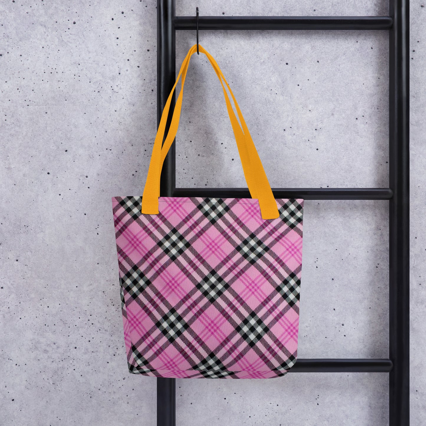 Pink and black trendy checkered tote purse with bright yellow straps hanging on black ladder