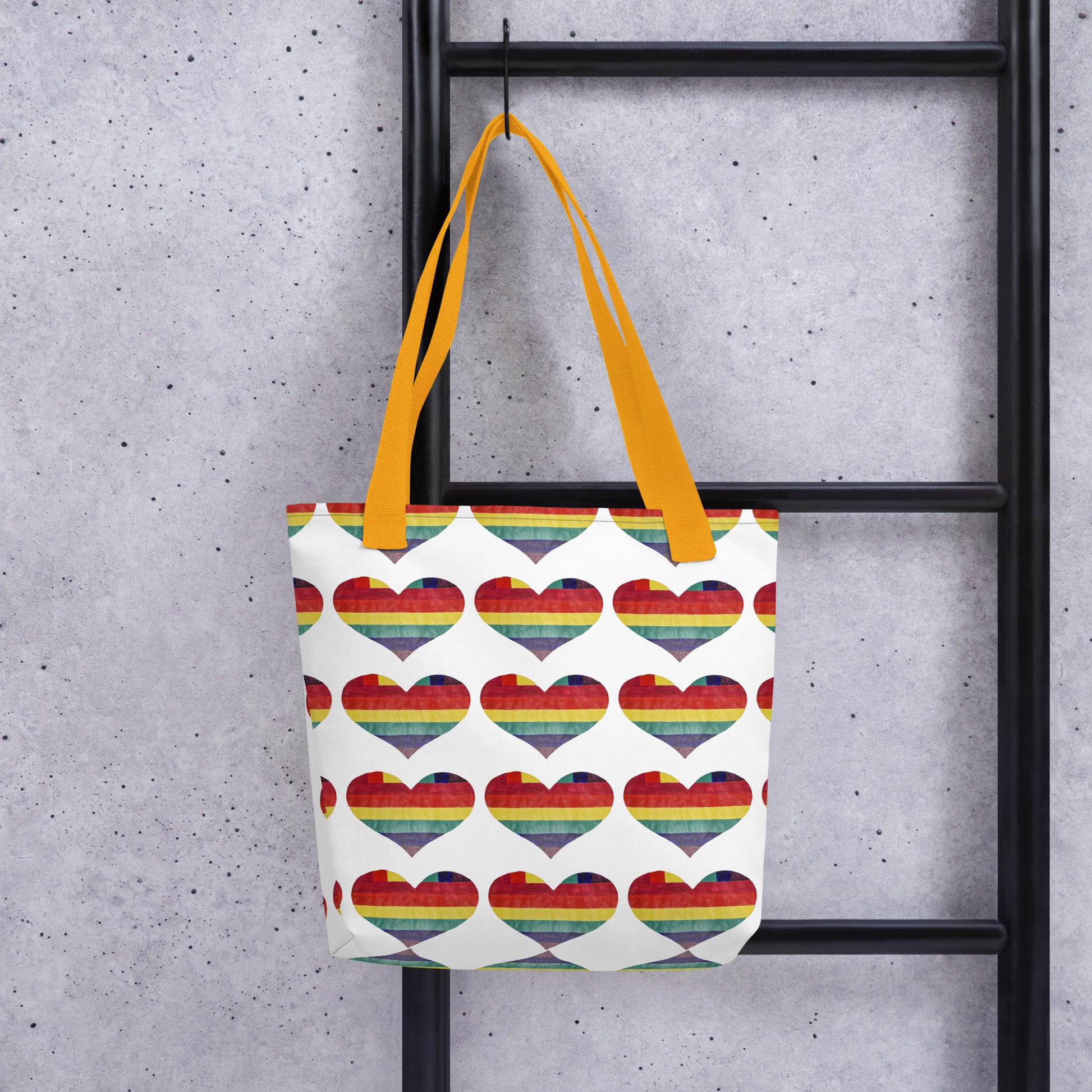 LGBT pride tote bag with rainbow heart pattern and yellow handles hanging on black metal ladder