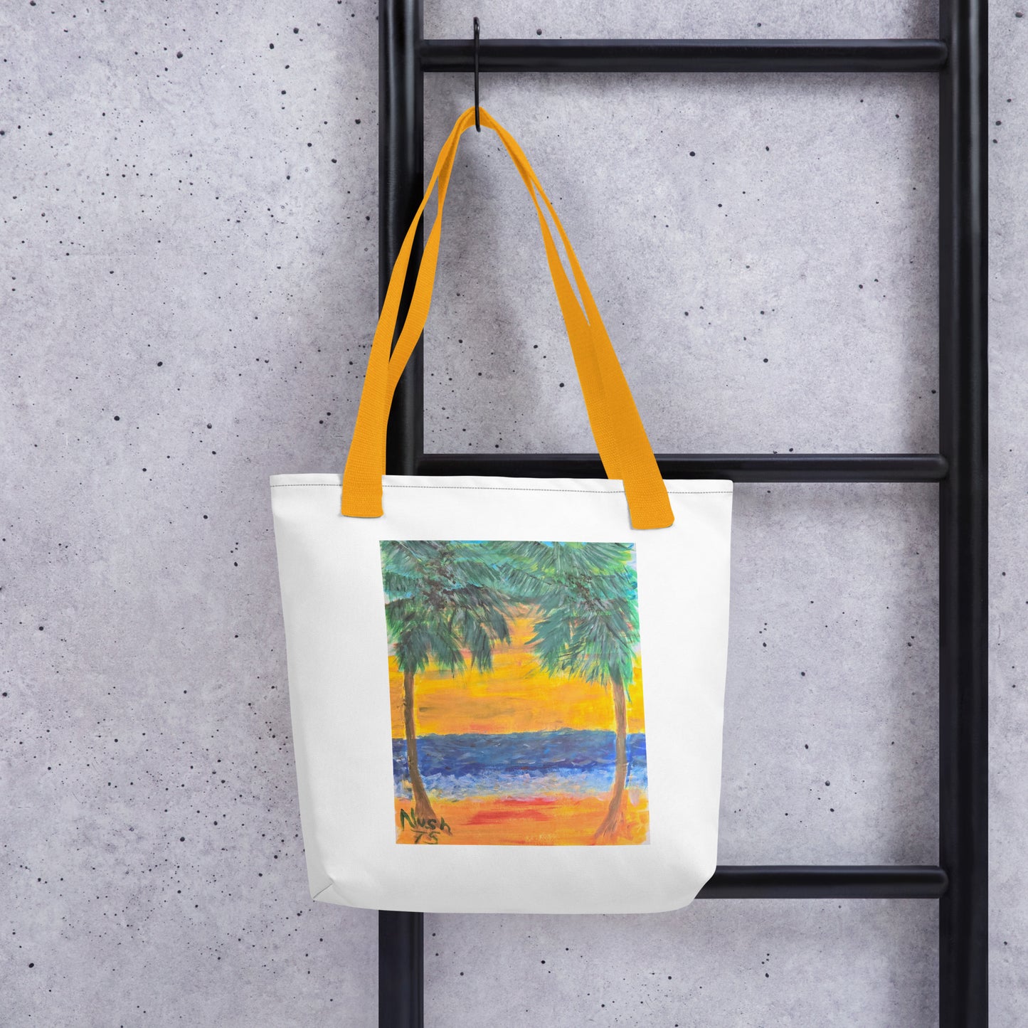 White beach tote bag with palm tree design and yellow handles hanging on black ladder