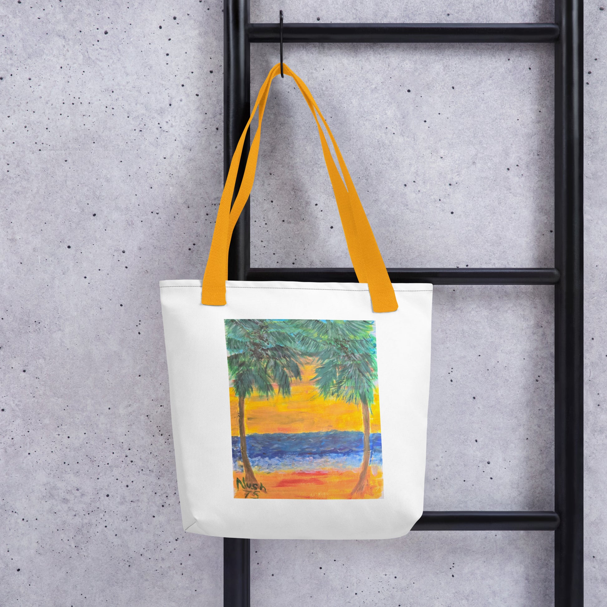 White beach tote bag with palm tree design and yellow handles hanging on black ladder