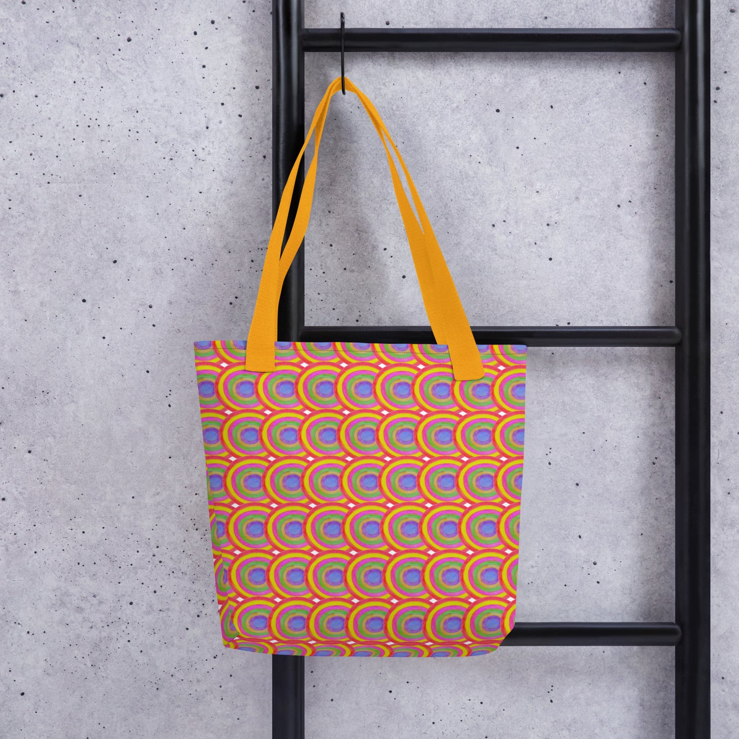Colorful boho tote bag for summer with orange handles hanging on black ladder against concrete wall