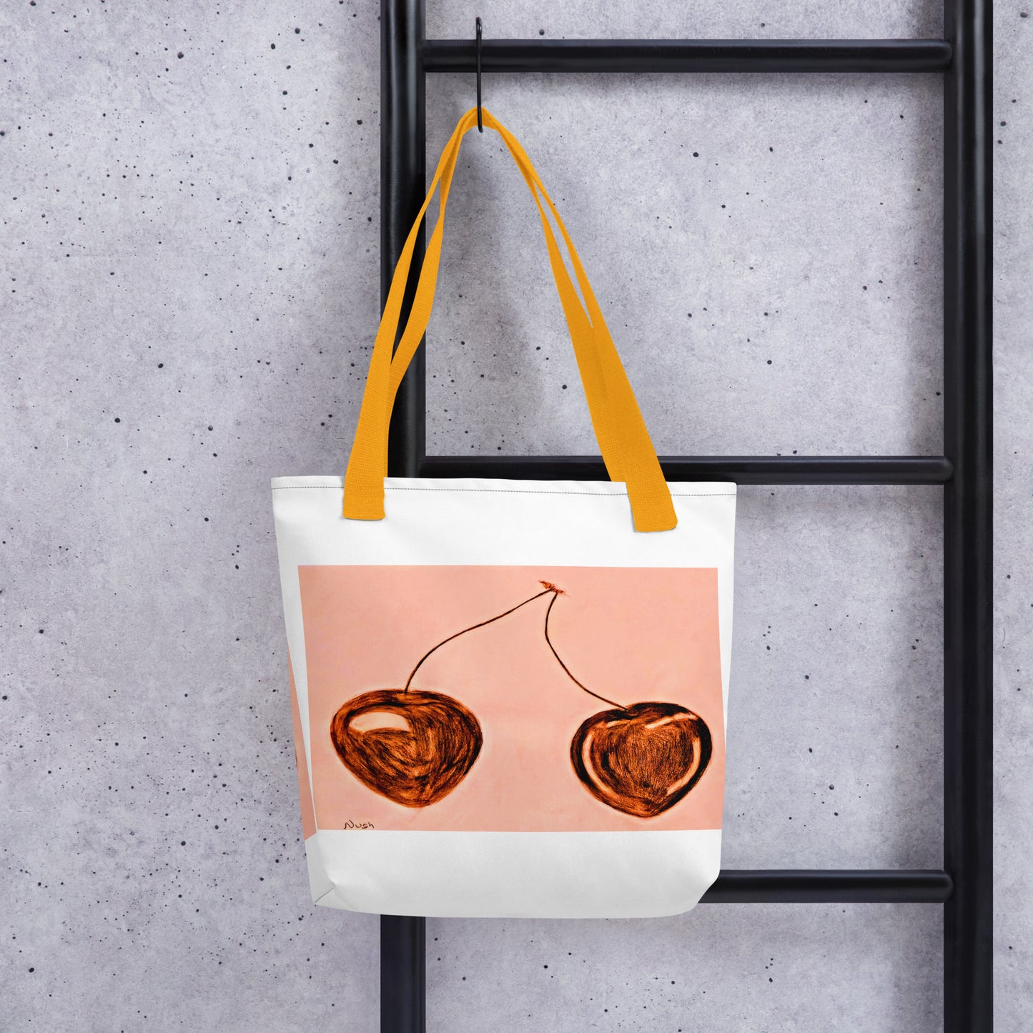 White cherry print tote bag with orange handles hanging on black ladder against gray wall
