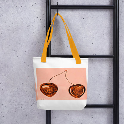 White cherry print tote bag with orange handles hanging on black ladder against gray wall