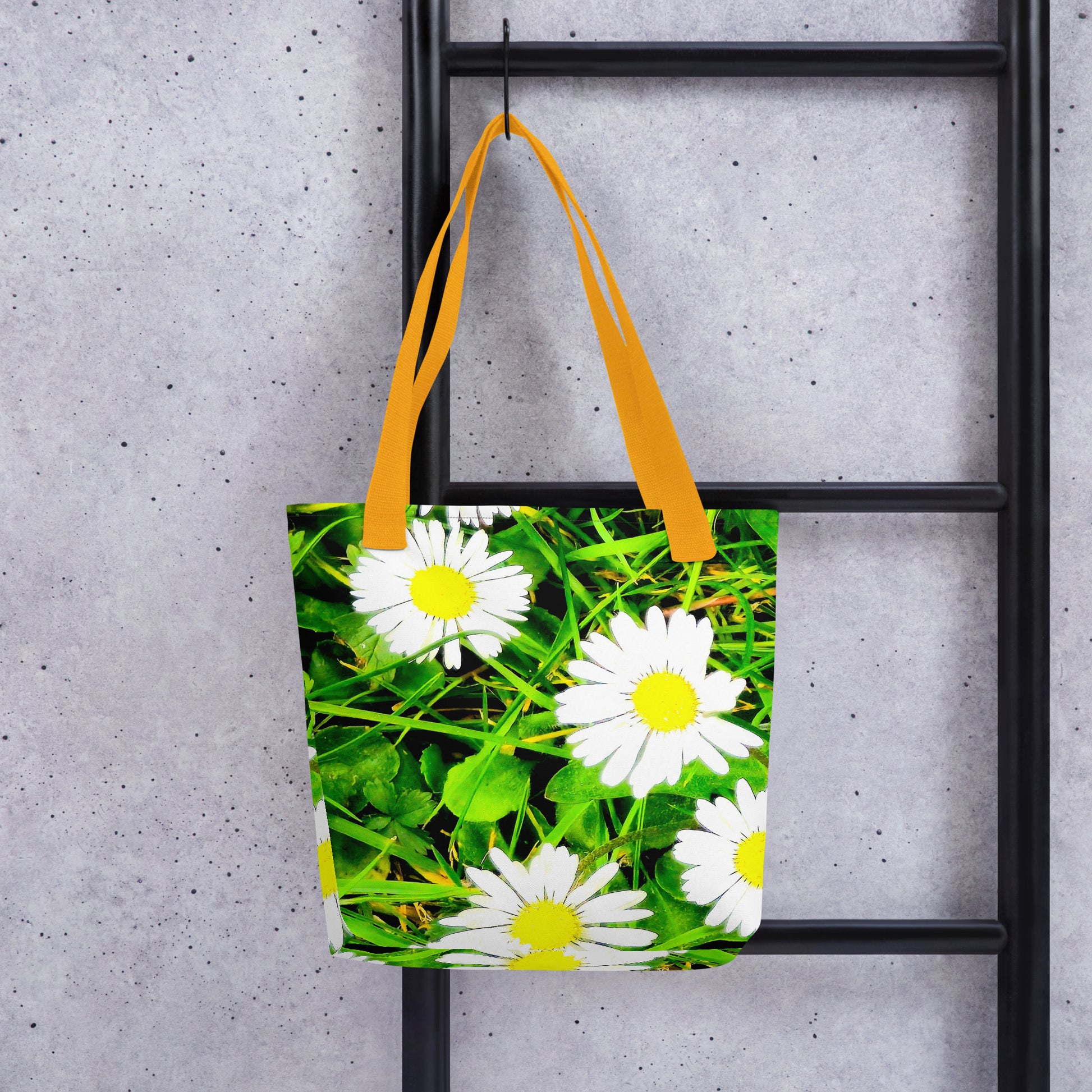 Daisy print tote bag with bright yellow handles hanging on black ladder against gray wall