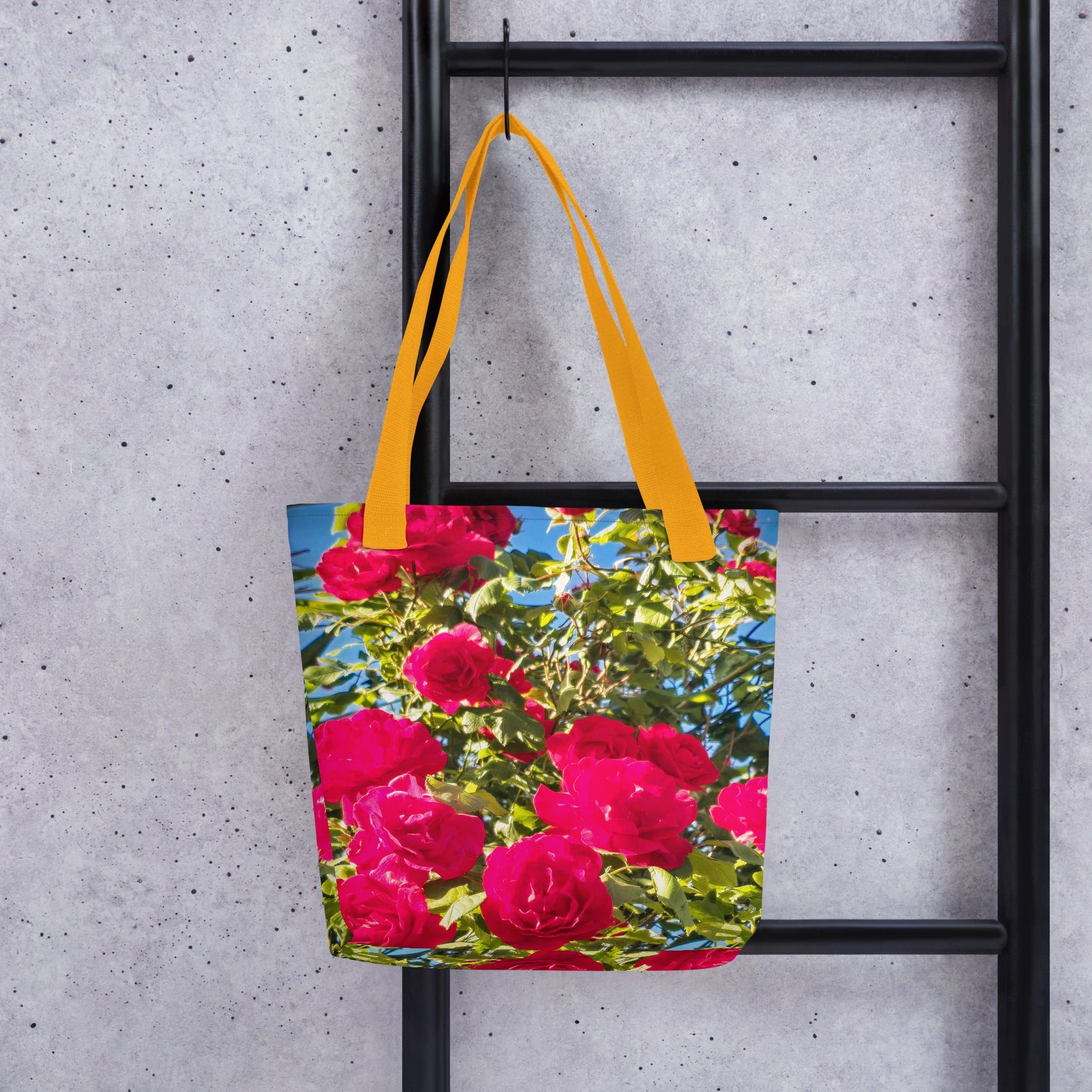 Eco-friendly summer beach bag ROSE PRINT with vibrant pink roses and yellow handles hanging on black ladder