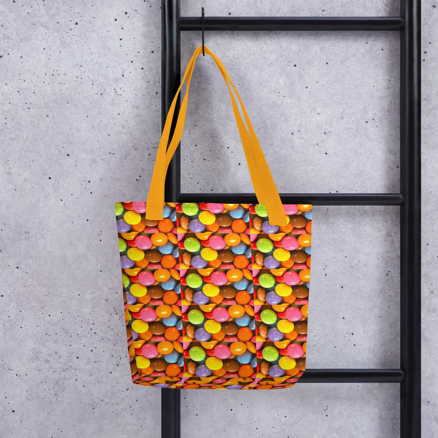 Fun patterned beach bag SMARTIES PRINT with colorful candy design and yellow handles hanging on black ladder