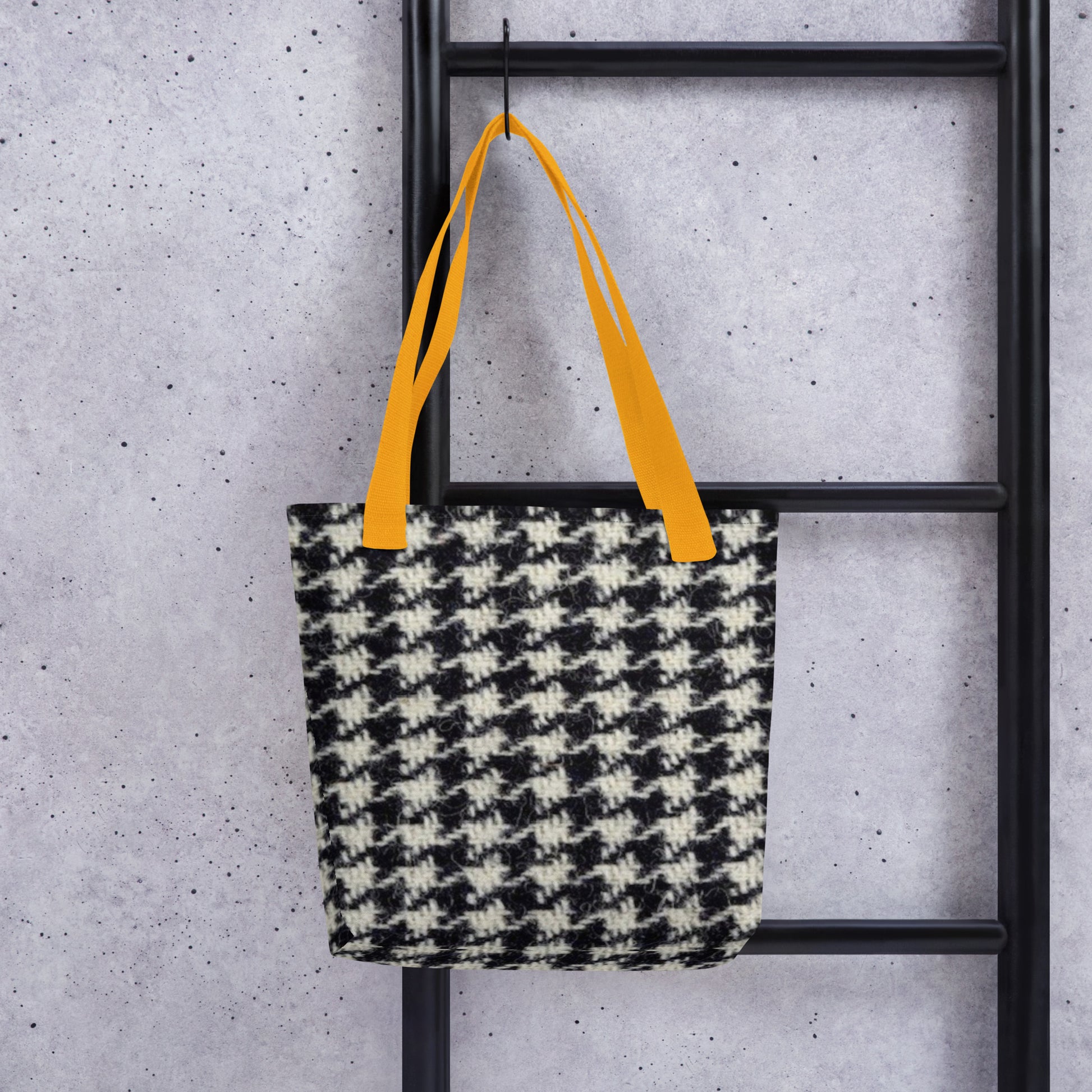 Black and white houndstooth tote bag with orange straps hanging on black ladder