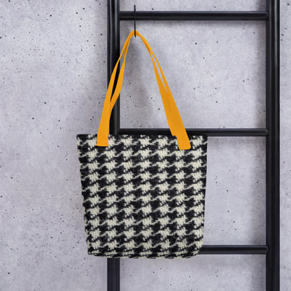 Black and white houndstooth tote bag with orange straps hanging on black ladder
