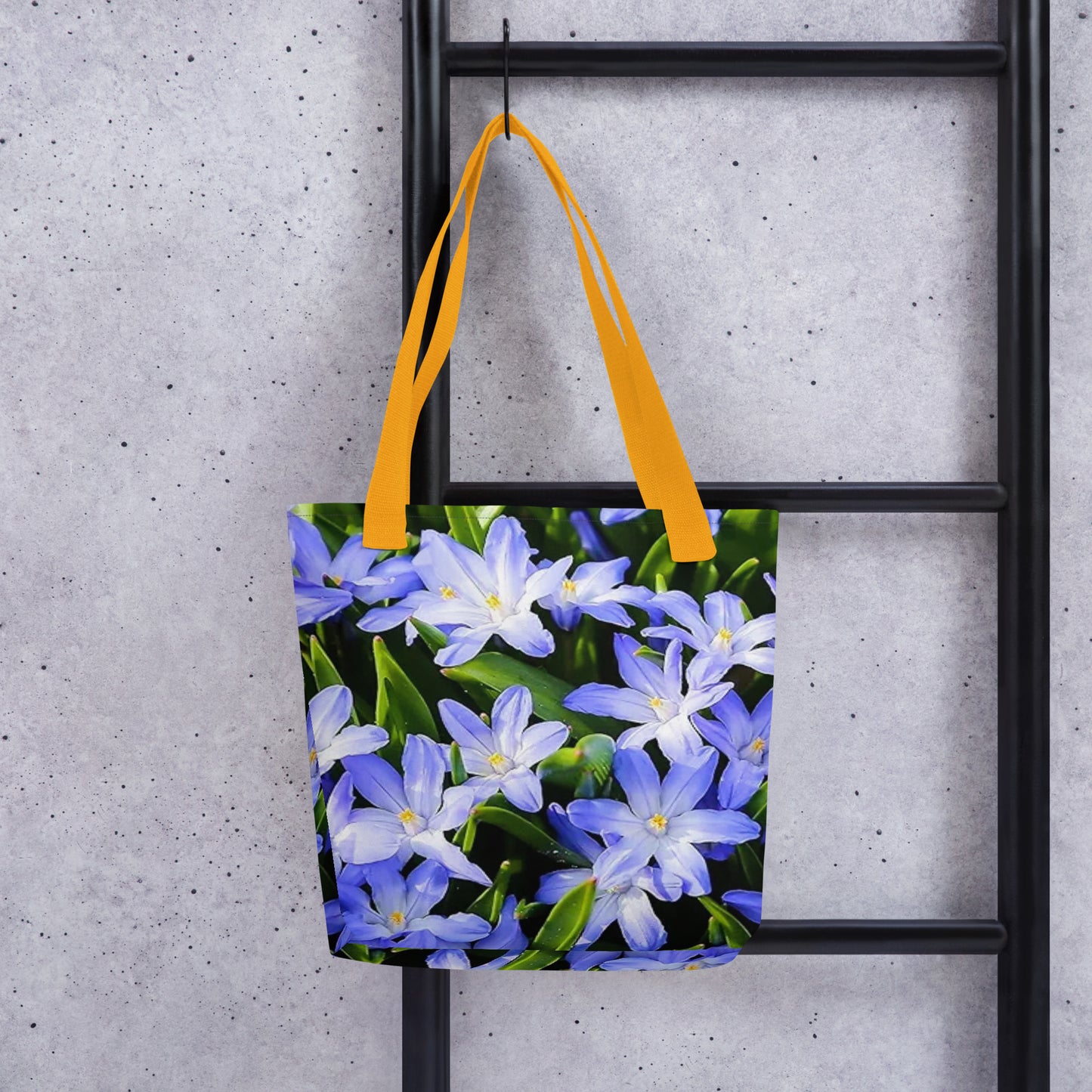 Large floral print tote bag with purple and white flowers and yellow handles hanging on black ladder