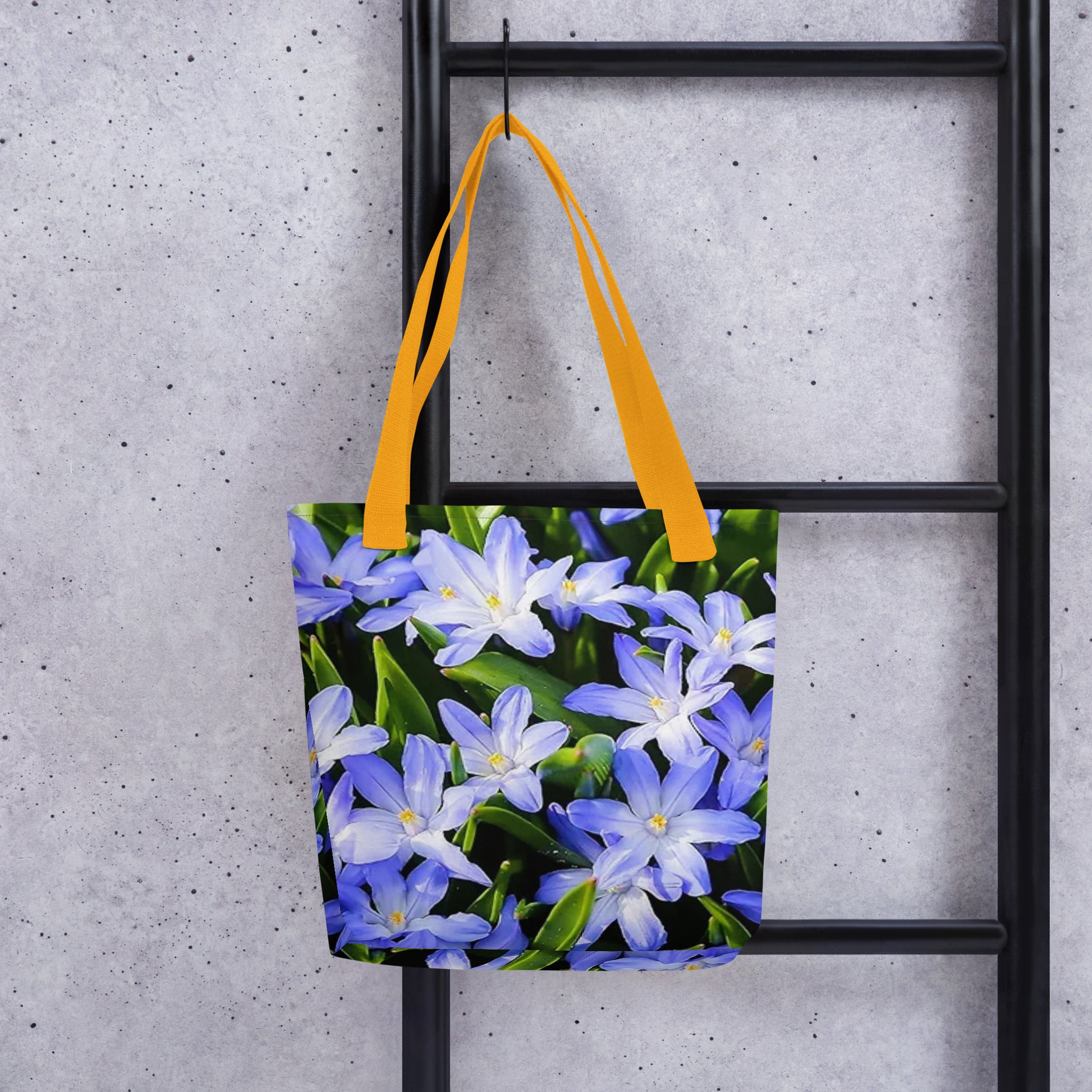Large floral print tote bag with purple and white flowers and yellow handles hanging on black ladder