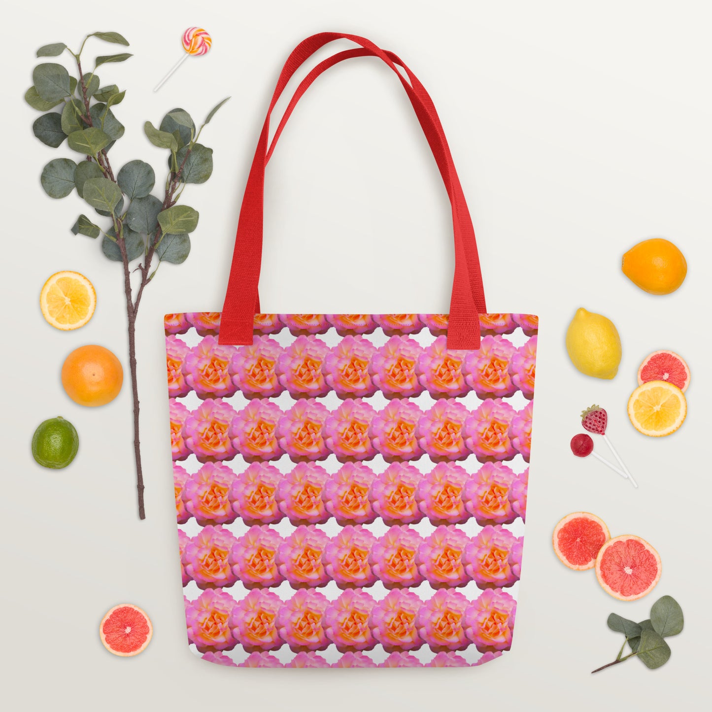 Pink flower print tote with red handles surrounded by citrus fruits and greenery