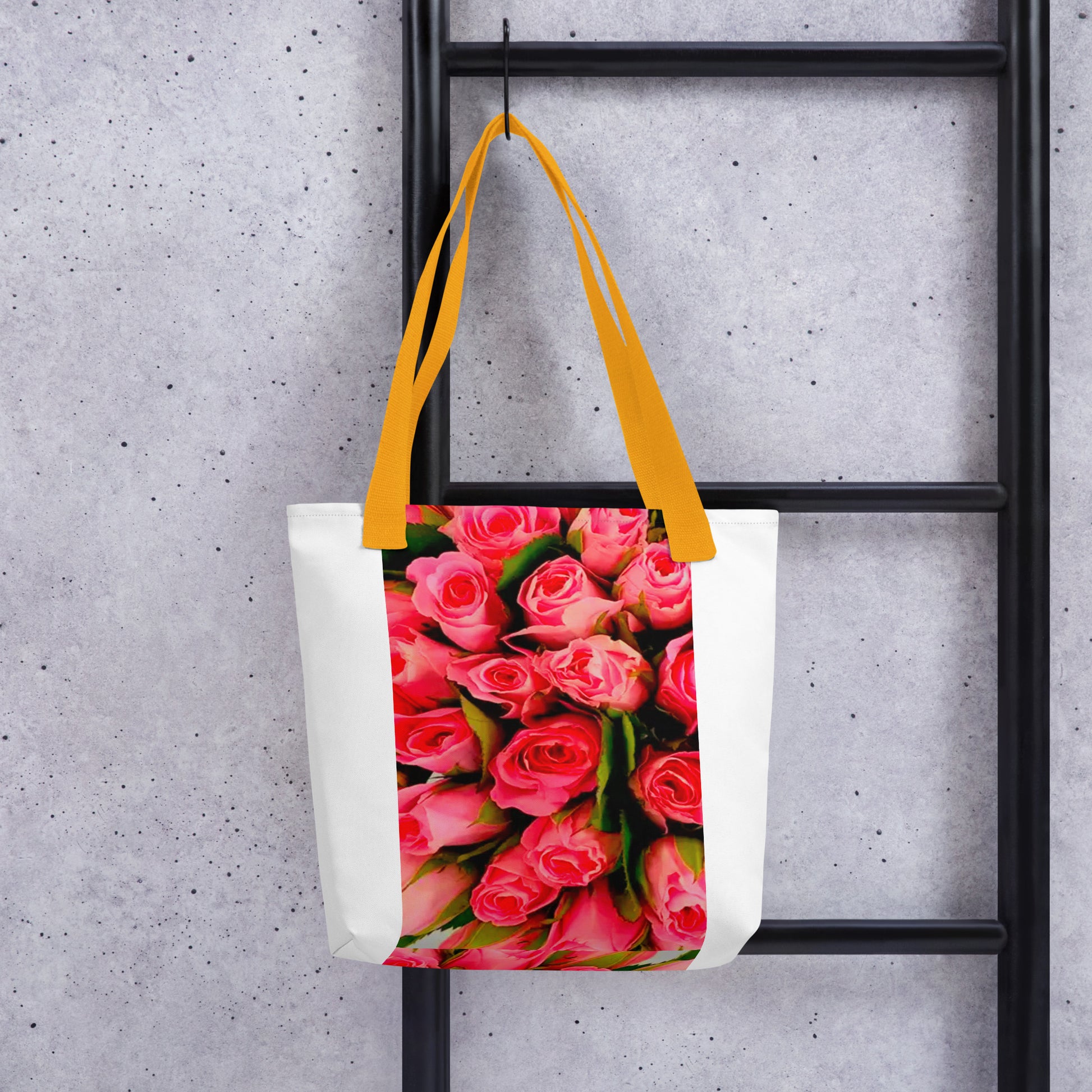 White tote bag with yellow straps featuring vibrant pink rose print bag design hanging on black ladder