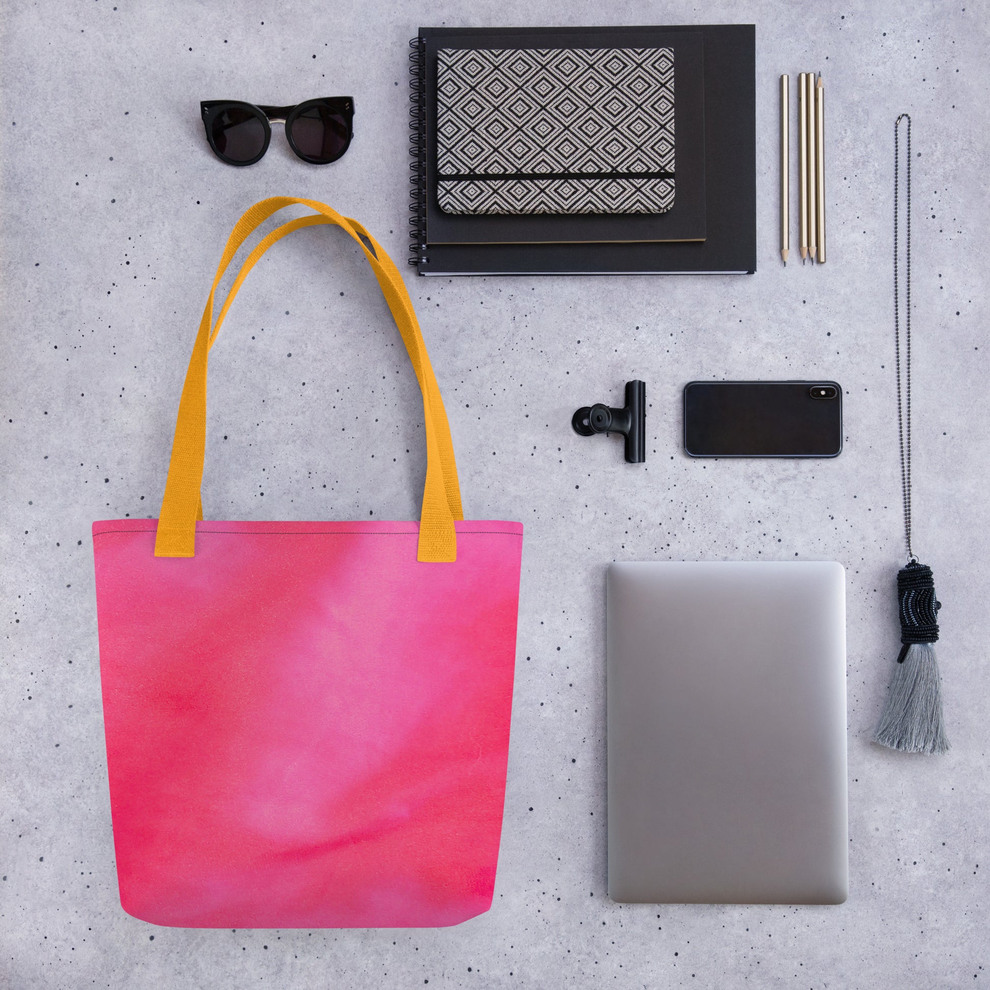 Pink tote bag for women with yellow straps surrounded by sunglasses, notebook, laptop, and phone