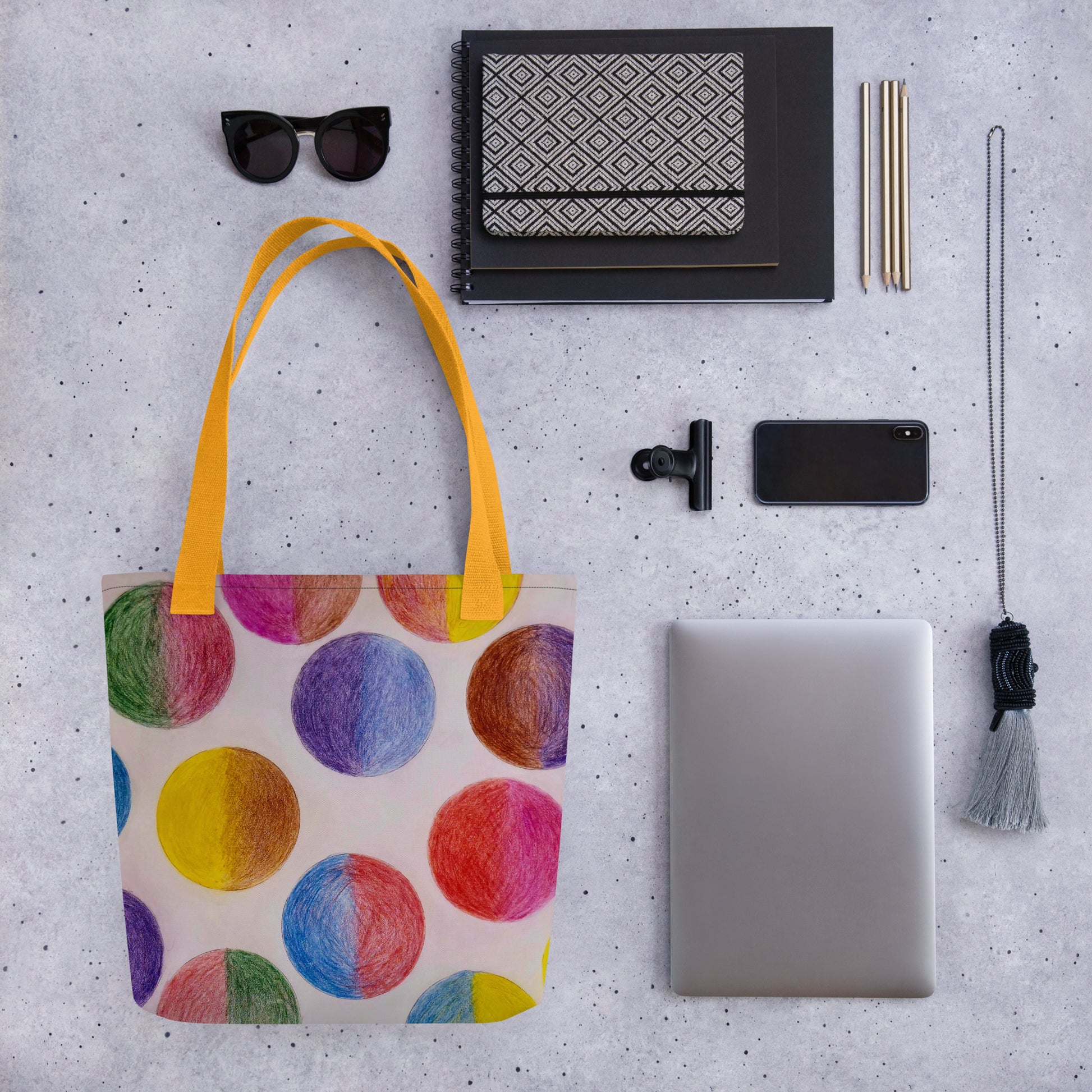 Colorful unique art print tote bag with yellow handles displayed with tech and stationery items