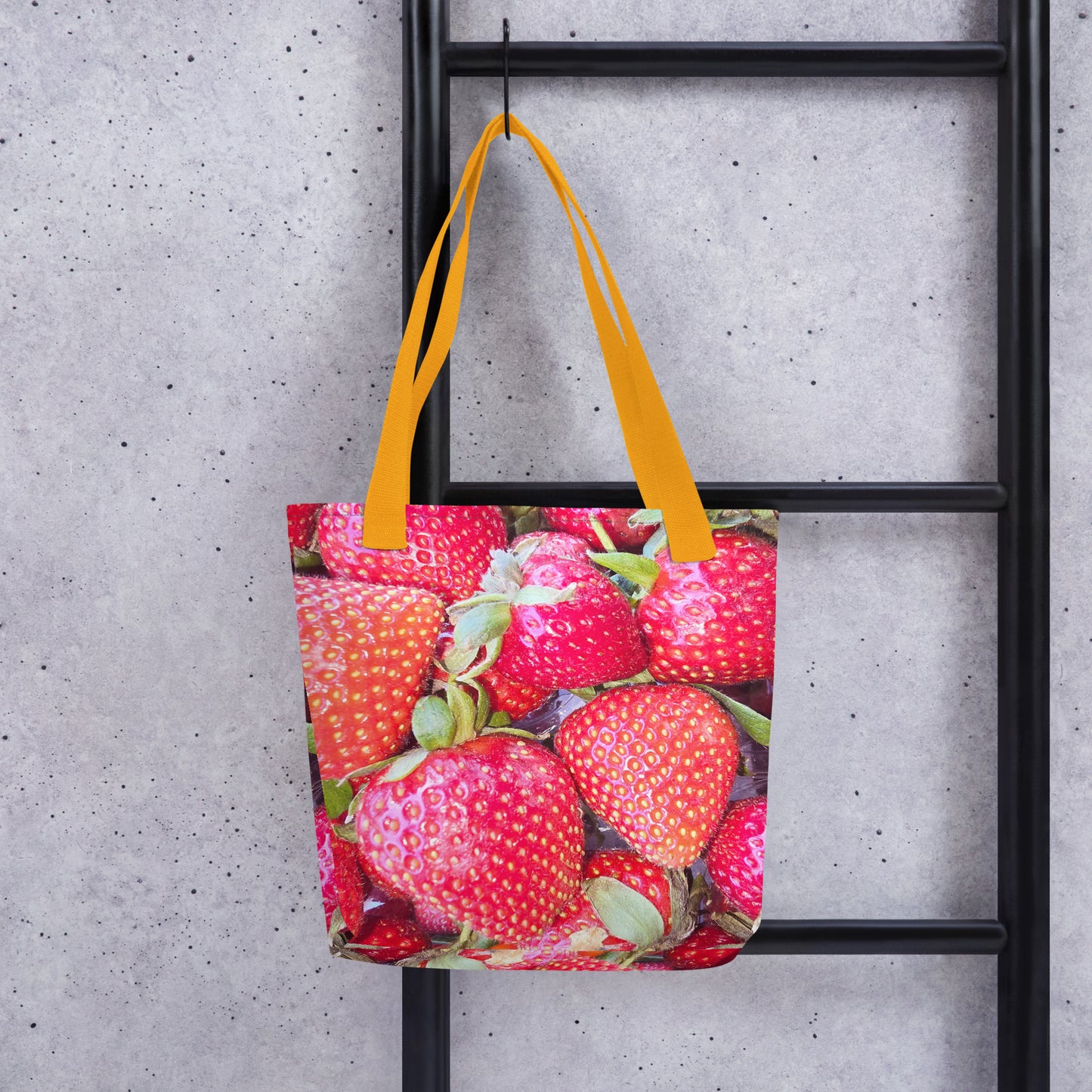 Strawberry print tote bag WIMBLEDON with vibrant red strawberries and yellow handles hanging on a black ladder
