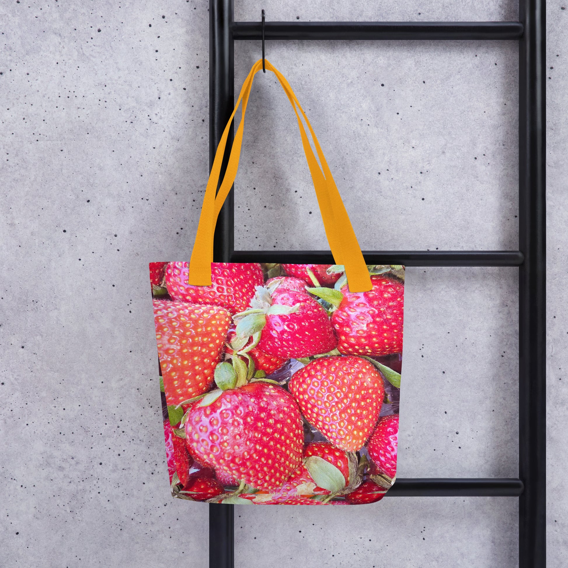 Strawberry print tote bag WIMBLEDON with vibrant red strawberries and yellow handles hanging on a black ladder